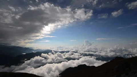 Sea of clouds spreads below mountain ridges under blue sky and sunlit clouds Stock Footage 339338779