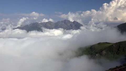 Sea of clouds surrounds sharp bare rocky peaks beneath blue sky and cumulus Stock Footage 339338691
