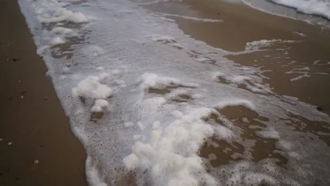 Sea foam being blown by the wind on sandy beach in slow motion. Spume flow Stock Footage 226820234