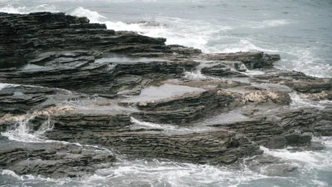Sea at high tide hitting the cliffs. Different layers of rock can be see. Video stock 169748365