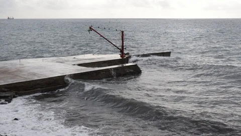 Sea moved in front of a red crane with strong waves against the pier of a sli Stock Footage 101925963
