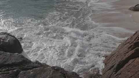 The sea moves against the rocks and sandy beach in slow motion Stock Footage