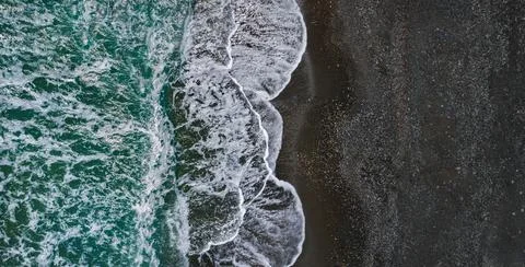Sea shore with dramatic texture of breaking waves and black sand, drone view Stock Photos