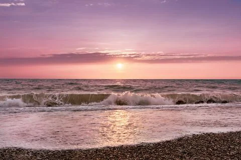 Sea splashing waves backlit by setting sun in front of beautiful sunset sky Stock Photos