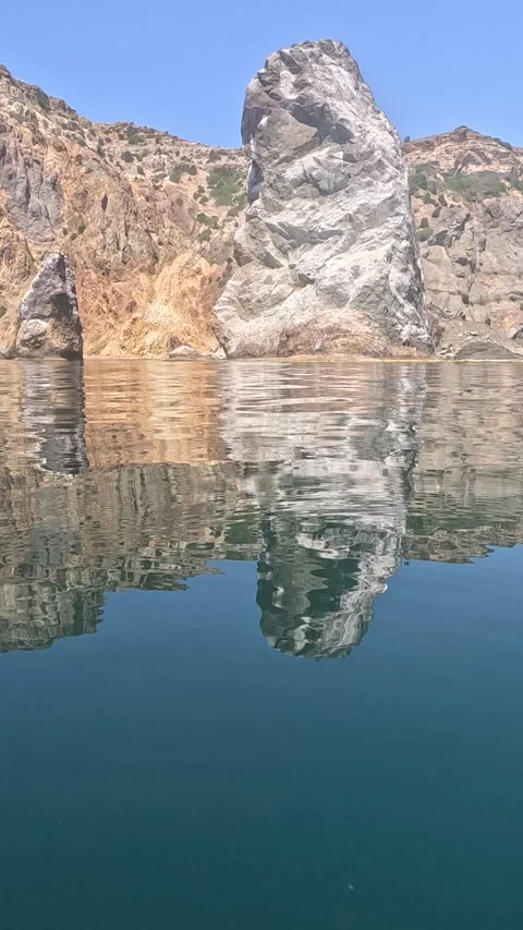 Sea stack, cliff, calm water reflecting large rock formation in clear blue water Stock Footage 320337471