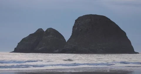 Sea stacks in the ocean with waves breaking along a beach during a cloudy day 库存影片 251502684