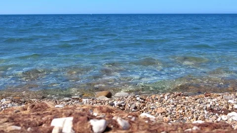 Sea stone pebble beach with clear blue water and small waves rolling to shore. Stock Footage 116181713