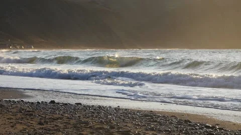 Sea surf glows in the rays of the rising sun against the backdrop of coastal hil Stock Footage 132167531