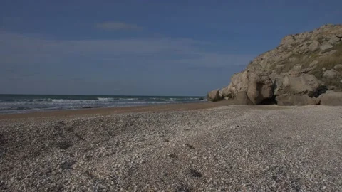 Sea surf on a shell beach under a blue sky and a rock on the horizon Stock Footage 132187106