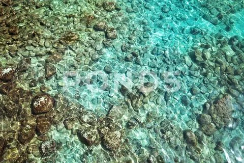 Sea water with sunlight on turquoise pebbles Stock Photos