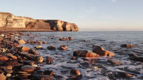 Sea water waves lapping at a rocky beach with cliff in the background. Stock Footage 169167277