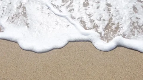 The sea wave gently rolls onto the clean golden sand, leaving white foam on the Stock Footage 318544922