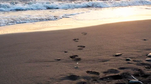 Sea wave rolls ashore Human footprints in the sand close-up sunrise or sunset Stock Footage 117538103