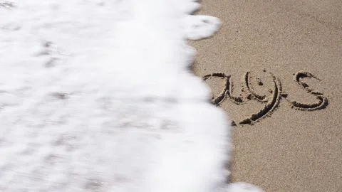 A sea wave washes away the text written on the sand from the beach - holidays Stock Footage 254428523