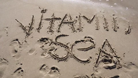 A sea wave washes away the text written on the sand from the beach - vitamin sea Video stock 255719312
