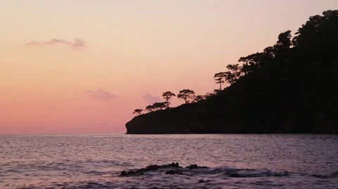Sea waves and peninsula silhouette with trees at sunset. Stock Footage 59777057