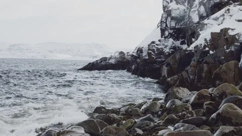 Sea waves are beating against snow-covered rocks. winter fjord in fog Stock Footage 322776530