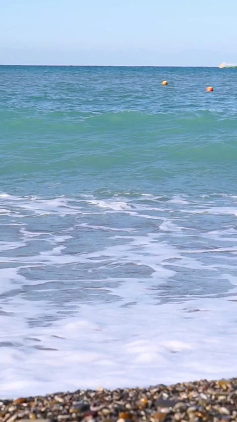 Sea Waves Breaking on Pebble Shore with Buoys in Background Stock Footage 346639378