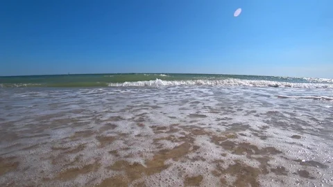 Sea waves cover a camera on a beautiful sandy beach on a sunny summer day. Video stock 87568415