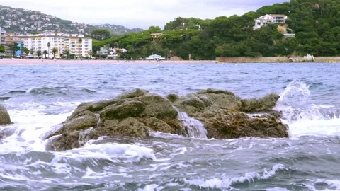 Sea waves crash on beach rocks in the evening with city and forest in background Stock Footage 161083238