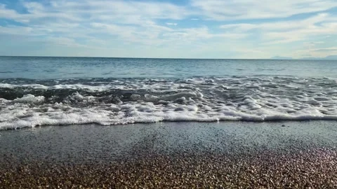 Sea waves gently splash on the beach at sunset, coloring the horizon with warm Stock Footage 264055055
