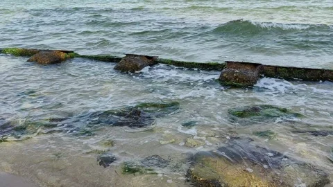 Sea waves gently wash over the moss-covered, rusted remnants of an old pier Vídeos de archivo 335045687