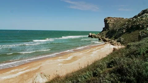 Sea waves hit the beach, a strong wind blows, and a steep cliff can be seen in Stock Footage 218405095