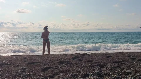 Sea waves hitting the shore of pebbles. Woman in the black bikini enjoys th.. Video stock 319694323