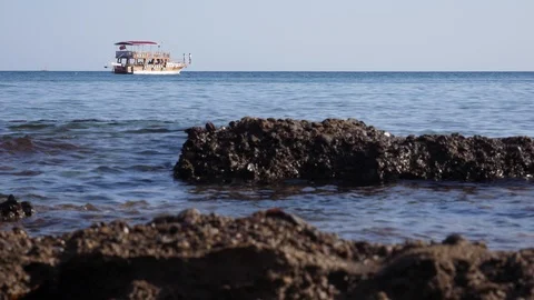 Sea waves lapping on rocks as boat sales past on horizon Stock Footage 98183776
