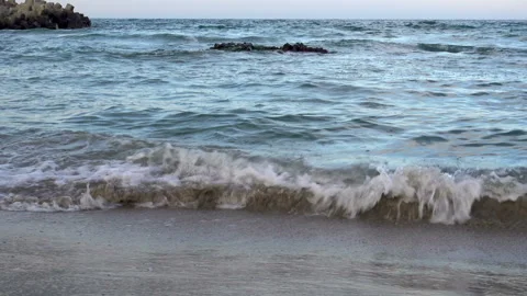 Sea waves passes through a small stone reef and sandy beach. Stock Footage 98395707