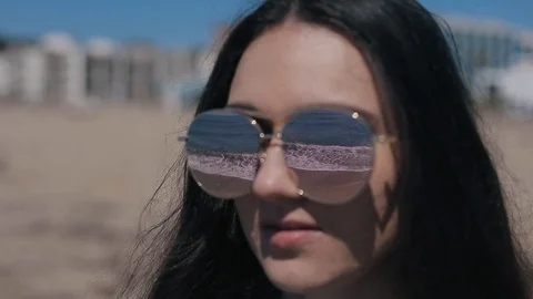 Sea waves reflected in the sunglasses of a beautiful brunette on the beach Stock-Footage 95944016