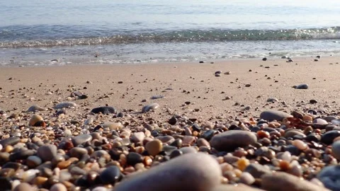 Sea waves ripple over a tranquil shoreline, where sand meets scattered pebbles Stock Footage 313656560