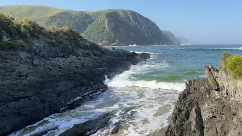 Sea waves rolling in between big beach boulders with mountain views Stock Footage 264012152