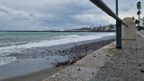 Sea waves rolling onto a pebble beach near a promenade Stock Footage 300242836