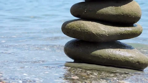 The sea waves rush to the shore and wash the lonely pyramid of stones standing Stock Footage 143399239