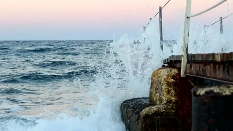 Sea waves with splashes break on the rocky shore on which the bridge is located Stock Footage 163201496