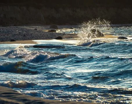Sea waves with splashes at sunset or sunrise. Ocean waves washing coast sand  Stock Photos