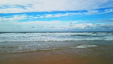 Sea waves wash the sandy beach. There is a blue sky with fluffy white clouds on Stock Footage 238084590