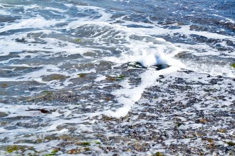 Seacoast waves. Sands and shells on the beach. Summertime seacoast. Ocean. Stock Photos