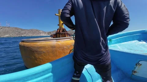 Seafarer securing a small boat to a yellow mooring buoy in tropical turquoise 動画素材 333761348