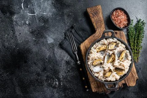 Seafood Risotto with clams in a skillet. Black backgroud. Top view. Copy space Stock Photos