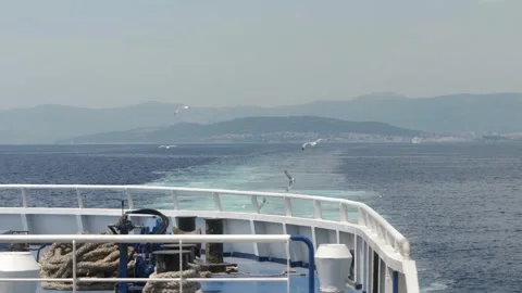 Seagulls fly after a ship as it departs the shore, leaving a trail on the water. Stock Footage 295213299