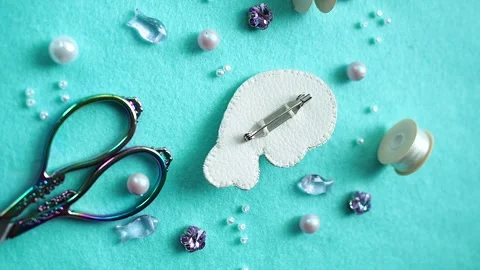 Seal brooch on a blue background fabric with beads, scissors, threads and pearls Stock Footage 248529341