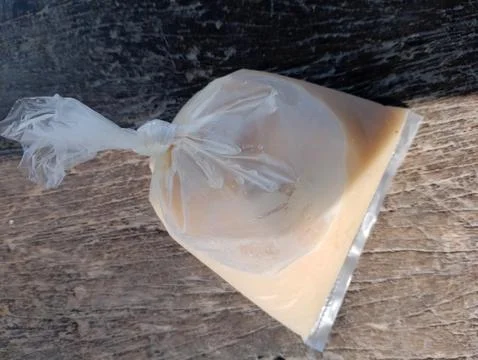 Sealed translucent plastic bag containing sweet milky liquid on wooden surfac Stock Photos