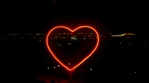 Seamless 4k single neon red heart on a black background, and bokeh city lights. Stock Footage 300324038