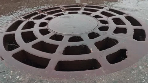 Seamless loop round manhole cover with a grid pattern, surrounded by water .. Stock Footage 319436806