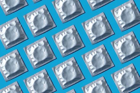 Seamless pattern of condoms in foil packaging on a blue background. Stock Photos