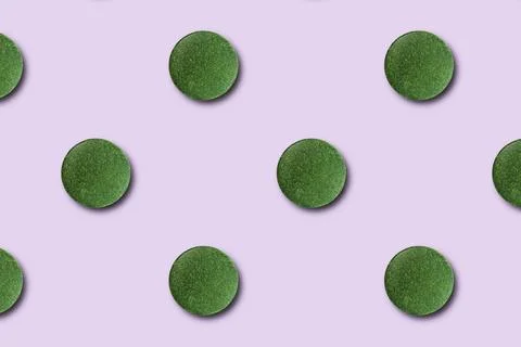 Seamless pattern of green chlorella or spirulina tablets on a pink background Stock Photos