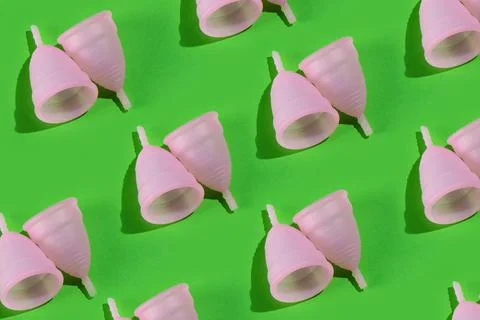 Seamless pattern of two pink menstrual cups on a bright green background. Stock Photos
