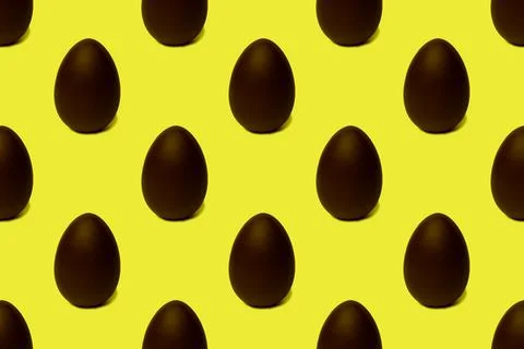 Seamless pattern of whole chocolate Easter eggs on a yellow background. Easte 스톡 사진